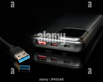 Schwarze tragbare Powerbank mit 100 Prozent Digitalanzeige, Reflexion und USB Type-A-Kabel auf schwarzer Oberfläche. Moderner externer Akku für Mobilgeräte Stockfoto