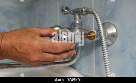 Die Hand eines Mannes legt ein Chrom-Fliegrad auf den installierten Ventilkörper eines Zweihebel-Mischers. Der zweite Hebel fehlt noch, sodass ein Messingdetail sichtbar wird Stockfoto