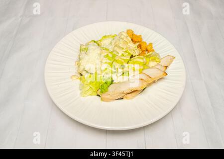 Gegrilltes Hühner-Cesar-Salat mit Römersalat, Croutons und geraspeltem Parmesan auf einer gerippten weißen Platte Stockfoto