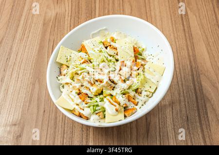 Caesar-Salat mit Hähnchen, Croutons, Käsescheiben, zerkleinertem Salat und cremiger Dressing in einer weißen Schüssel Stockfoto