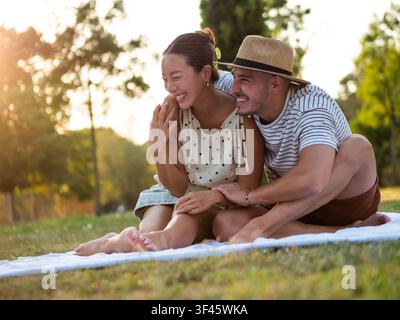 Ein multikulturelles Paar teilt einen zarten Moment während eines Picknicks bei Sonnenuntergang im Park. Stockfoto