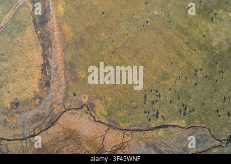 Windinges trockenes Flussbett, das sich durch arides Gelände schlängelt, und zeigt die Auswirkungen des Klimawandels und der schweren Dürre auf die Natur. Abstrakte Erdtextur mit organischem Naturmuster und Kopierraum. Stockfoto
