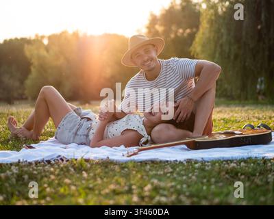 Ein fröhliches junges Paar entspannt sich auf einer Picknickdecke in einem friedlichen Park während der goldenen Stunde. Stockfoto
