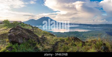 Panoramablick vom Berg Batur in Kintamani, Bali, mit dem Batursee, schwarzen Lavafeldern, den Trunyan-Hügeln und dem fernen Berg Agung unter dramatischer Beleuchtung Stockfoto