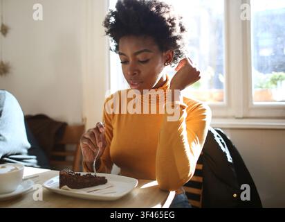 Junge schwarze Frau isst Kuchen in einem sonnigen Café Stockfoto