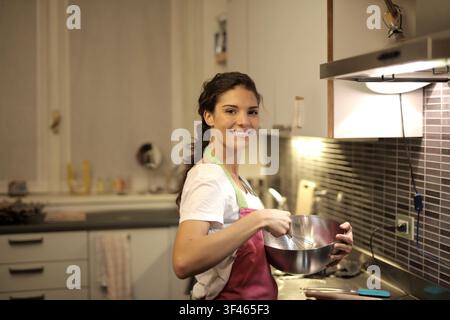 Lächelnde Frau, die Zutaten in einer Küchenschüssel schlägt Stockfoto