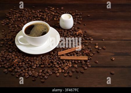 Tasse mit schwarzem Kaffee mit gerösteten Kaffeebohnen, Vanilleschoten und Sternanis auf Holztablett Stockfoto