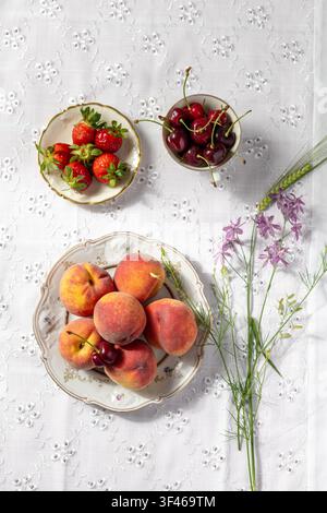 Frische Sommerfrüchte und Blumen auf Spitzentischdecke Stockfoto