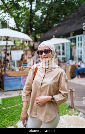 Stilvolle muslimische Frau trägt Hijab und Sonnenbrille auf einem Markt im Freien in Bali, Indonesien. Reise- und modernes Lebensstilkonzept. Stockfoto