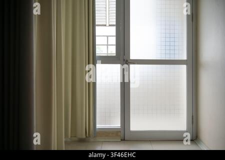 Mattscheibentür mit geometrischem Muster neben beigefarbenen Vorhängen in einem sauberen Innenraum. Sanftes natürliches Licht schafft einen minimalistischen architektonischen Hintergrund Stockfoto