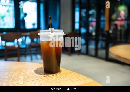 Erfrischender Eiskaffee serviert in einem Plastik-To-Go-Becher auf einem Holztisch in einem modernen Café. Getränke- und Lifestyle-Konzept mit Platz für Text. Stockfoto