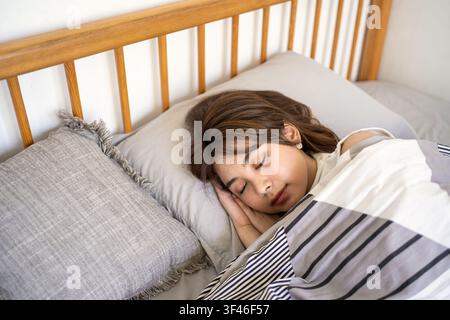 Nahaufnahmeporträt einer indonesischen Frau, die friedlich unter einer Decke schläft und gesunden Schlaf, Ruhe und Wohlbefinden symbolisiert. Stockfoto