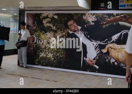 Dior-Werbeplakat mit männlichem Model in einer natürlichen, blumigen Umgebung, angezeigt in einer japanischen U-Bahn-Station. Ein junger Mann schaut auf sein Ph Stockfoto