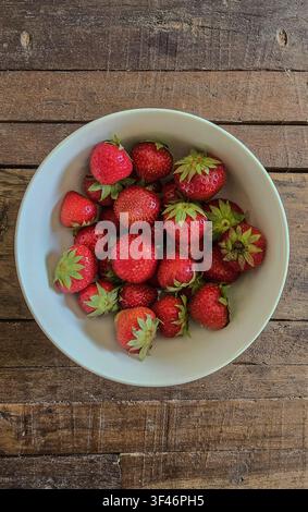 Frische rote Erdbeeren in einer weißen Schüssel auf einem dunklen Holztisch Stockfoto