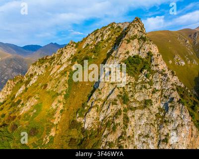 Luftaufnahme zeigt eine raue Berglandschaft in Kirgisistan. Steile felsige Hänge sind mit Flecken trockenen Grases und grüner Büsche geschmückt, die zu Stockfoto