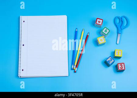 Leeres Notizbuch mit bunten Stiften und Alphabetblöcken auf blauem Hintergrund mit Kopierraum Stockfoto