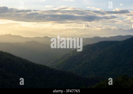 Ein üppiger grüner Bergrücken bei Sonnenuntergang mit geschichtetem bewaldetem Tal und goldenem Himmel, der friedliches atmosphärisches Licht erzeugt Stockfoto