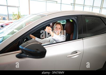 Zufriedene Frau hält Autoschlüssel in der neuen Fahrzeugausstellung Stockfoto
