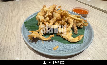 Knusprig gebratene Tintenfischringe, serviert auf einem mit Bananenblatt ausgelegten Teller mit scharfer Dip-Sauce. Stockfoto
