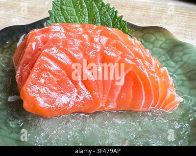 Frische Thunfisch-Sashimi-Scheiben, gekühlt auf zerstoßenem Eis mit Shiso-Blättern auf einem dekorativen japanischen Teller serviert. Stockfoto
