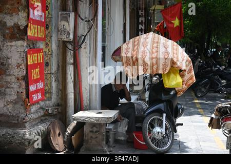 Vietnamesischer Verkäufer sitzt auf der Straße unter einem farbenfrohen Sonnenschirm im alten Viertel von Hanoi, Vietnam Stockfoto