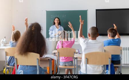 Verschiedene Schüler heben die Hand, um während des Mathematikunterrichts der Lehrerin zu antworten Stockfoto