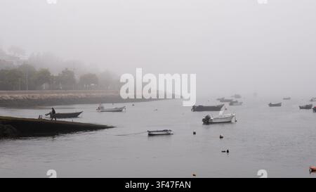 Kleine Boote verstreut auf ruhiger Wasserfläche im dichten Nebel der Atlantikküste Portugals Stockfoto