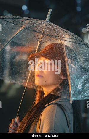 Frau mit geschlossenen Augen, die unter einem leuchtenden Regenschirm Schutz sucht, Shanghai, China Stockfoto