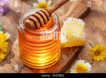 Natürlicher Bio-Honig im Glasgefäß, Honiglöffel und Waben sind in der Nähe. Natürlicher Lebensmittelhintergrund. Stockfoto