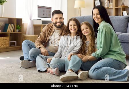 Eltern mit zwei Töchtern, die auf dem Wohnzimmerteppich sitzen und zu Hause lächeln Stockfoto