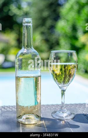 Flasche und zwei Gläser Weißwein auf einem Außentisch in der Nähe des Resort-Schwimmbeckens. Stockfoto