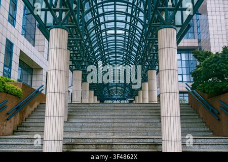 Eine moderne architektonische Struktur mit einem Glasdach und Steintreppen. Die Szene zeigt ein symmetrisches Design und Grünpflanzen an den Seiten. Stockfoto