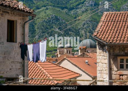 Eine malerische Ansicht traditioneller Steinhäuser mit Ziegeldächern. Wäsche hängt an einer Leine, grüne Berge und Kuppelgebäude im Hintergrund. Stockfoto