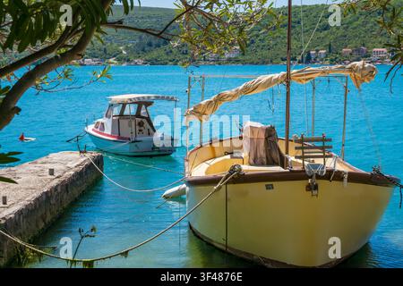Zwei Boote, die in einem ruhigen Hafen festgemacht sind. Eines ist ein Holzfischerboot, das andere ein kleines Motorboot. Klares blaues Wasser und üppige Grünpflanzen umgeben die Szene. Stockfoto