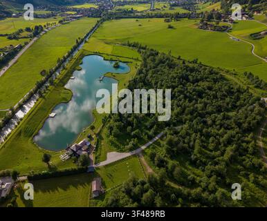 Luftbild einer kleinen Seenlandschaft, die von dichtem Wald und grünen Ackerflächen in Österreich umgeben ist, mit gewundenen Wegen, ländlichen Gebäuden und einem Dorf im Tal Stockfoto