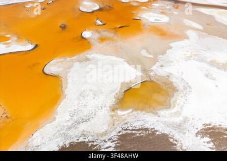 Luftaufnahme einer abstrakten Salzlagune im Altiplano mit lebhaftem orangefarbenem Mineralwasser und weißen Salzkrustenmustern, fotografiert im Salar de Pujsa Stockfoto