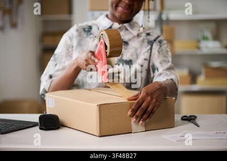Schwarze Frau versiegelt einen Versandkarton für die Erfüllung einer Kleinbestellung Stockfoto