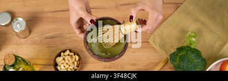 Hände vermischen lebendigen Matcha-Pulver mit Wasser unter Verwendung eines traditionellen Schneebesens und fördern damit das Wohlbefinden. Stockfoto