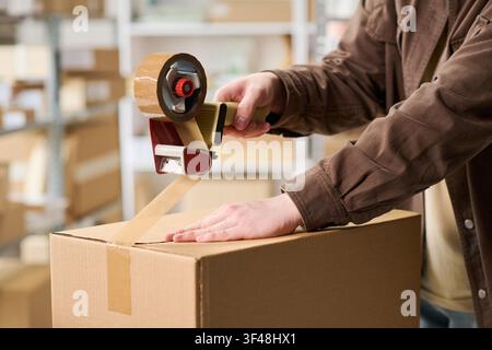 Erwachsener Arbeiter versiegelt eine Pappschachtel für die Versandabwicklung Stockfoto