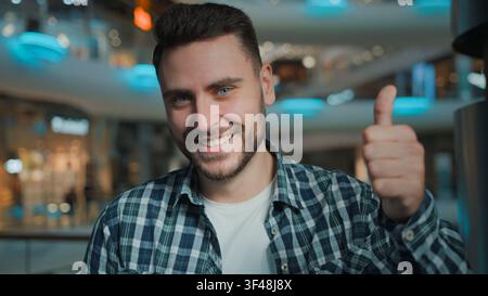 Zufriedener kaukasischer Mann zeigt Daumen hoch, lächelt in die Kamera und empfiehlt einen Rabatt im Einkaufszentrum, Geschäftsmann, Kunde, optimistisch Stockfoto