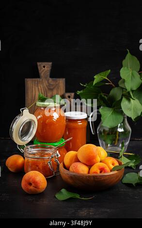 Frische Aprikosen und Aprikosenkonfitüre auf rustikalem dunklem Hintergrund Stockfoto