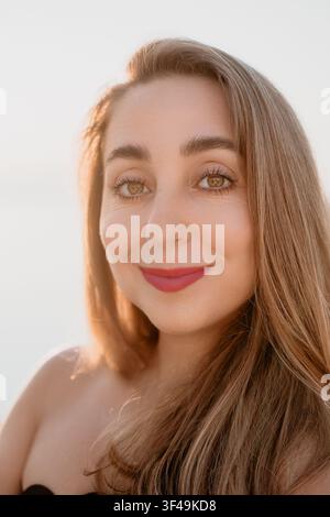 Frauenporträt Lächeln Nahaufnahme eines Porträts einer Frau mit langen Haaren, die im Freien unter warmem Goldstundlicht lächelt Stockfoto
