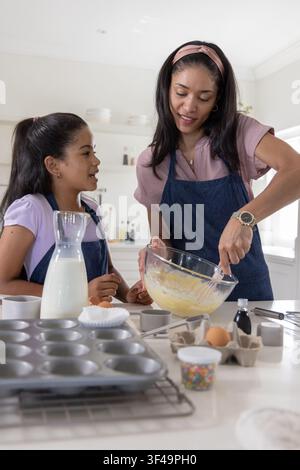 Afroamerikanische Mutter und Tochter rühren Teig in der Küche, tragen Jeansschürzen, Rührschüssel Stockfoto