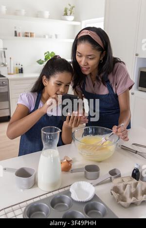 Afroamerikanische Mutter und Tochter rühren Teig in einer Schüssel mit Schneebesen und Smartphone in der Küche Stockfoto
