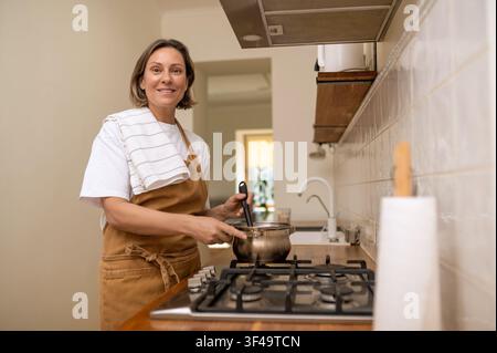 Lächelnde Frau mittleren Alters mischt Essen in einem Topf Stockfoto