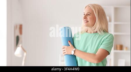 Lächelnde reife Frau hält eine blaue Yogamatte, Fitness und gesunder Lebensstil für Senioren, Heimtraining Stockfoto
