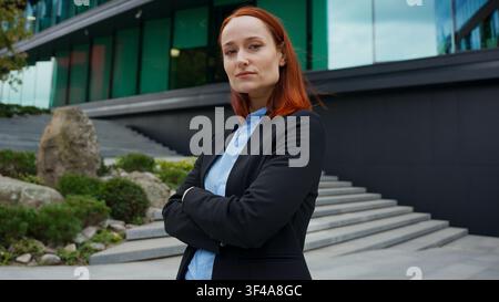 Porträt einer starken, selbstbewussten kaukasischen Geschäftsfrau in einer Stadt, Hände gekreuzt, Pose ernst, rothaarig, outdoor, erwachsene Frau, modern, urban Stockfoto