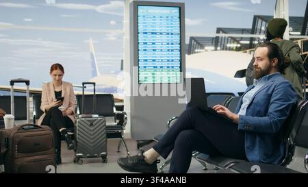Geschäftsmann nutzt Laptop und überprüft Smartphone, wartet während einer Geschäftsreise am Flughafen, bereit für den internationalen Flug. Der Delegierte Unternehmensmanager am Hauptsitz, modernes Reisen. Stockfoto