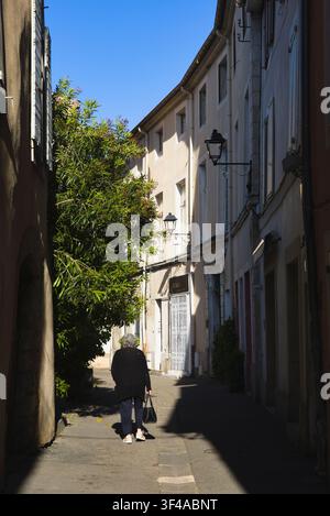 Ein Fußgänger geht eine schmale, schattenreiche historische Gasse im Dorf L'Isle-sur-la-Sorgue in der Provence in Südfrankreich hinunter. Stockfoto