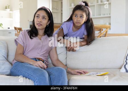Afroamerikanerin und Jugendlicher sitzen auf dem Sofa im Wohnzimmer, halten ein gelbes Heft und schauen nach oben Stockfoto